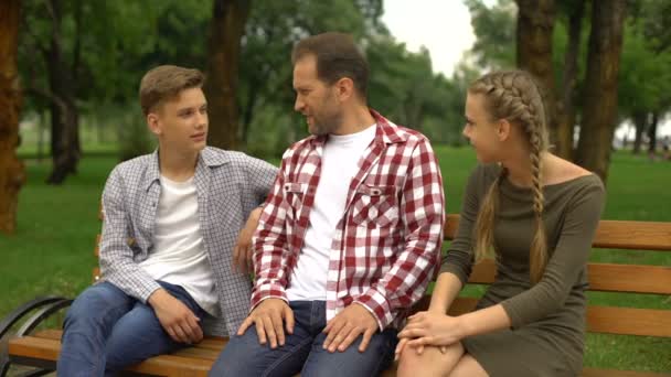 父亲和他十几岁的孩子在公园的长椅上说话 放松一下 — 图库视频影像