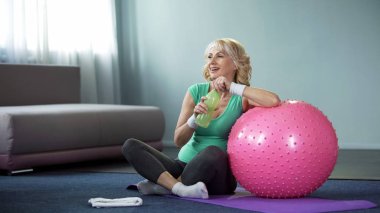 Memnun kadın kıdemli şişe su spor egzersiz yaptıktan sonra rahatlatıcı