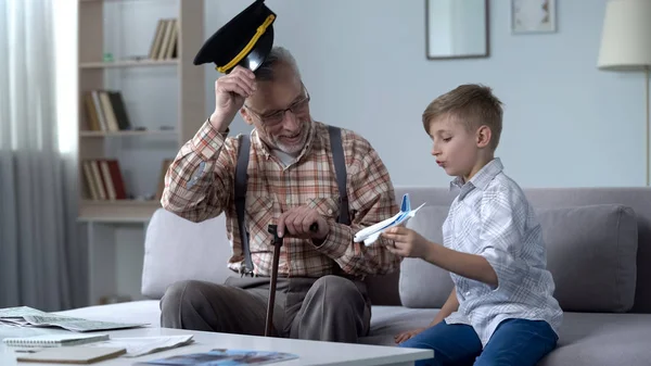 孙子玩玩具飞机 祖父在帽子敬礼小飞行员 — 图库照片