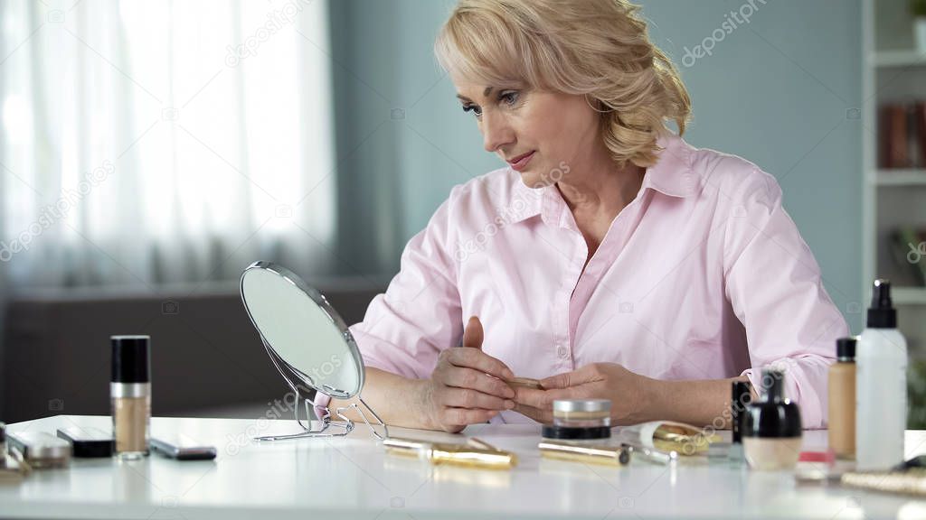 Elegant senior lady looking in mirror on table, anti-wrinkle collagen cosmetics