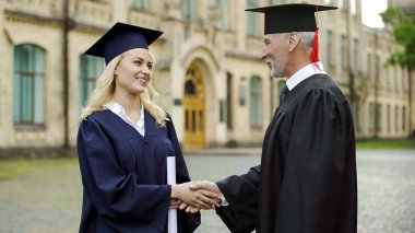 Tebrik ve el sallayarak öğrenci için diploma veren Üniversitesi Rektör