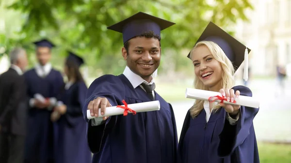 卒業証書を示し 笑みを浮かべて 男性と女性の卒業生が高等教育を完了します — ストック写真