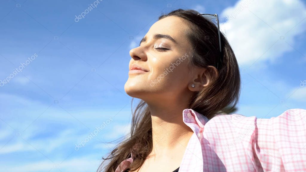 Pretty female enjoying sunshine, relaxing with eyes closed outdoors, holiday