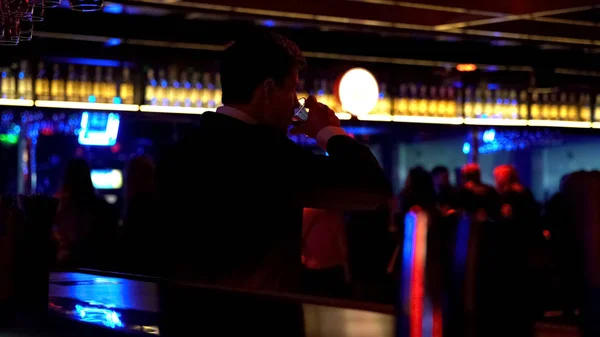 Man dancing alone at bar counter and drinking alcohol, watching people in club