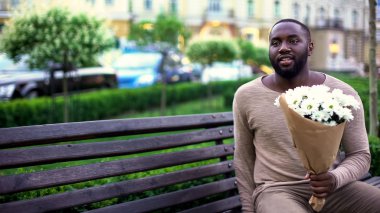 Kız arkadaşı, beklenti bekleyen siyah adam banktaoturuyor, çiçekli