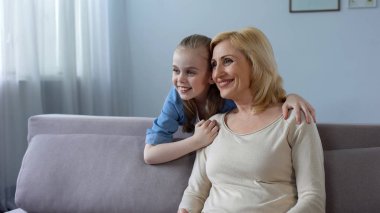 Kanepeye, mutlu bir aile oturan sarışın kadın çocuk sarılma Büyükanne