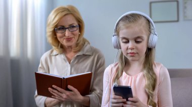 Büyükanne okuma kitabı ve kulaklık, ses dinleme çocuk bakarak kavramı