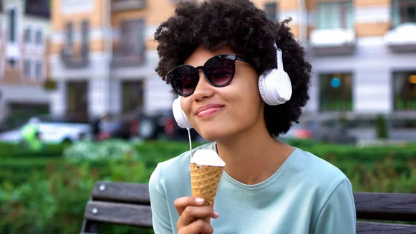 インスピレーションの女性 ヘッドフォンで音楽を楽しむレジャーのベンチにアイスクリームを食べること — ストック写真