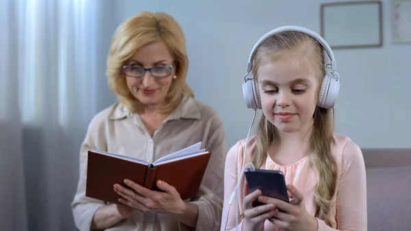 Kleines Mädchen Mit Kopfhörern Hört Buch Von Älterer Oma Lesen — Stockfoto