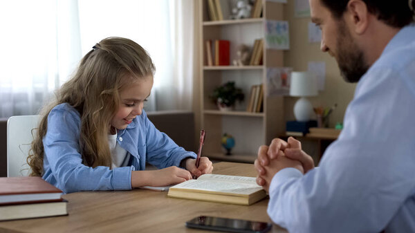 Smart daughter writing in exercise book, caring daddy is proud of his kid