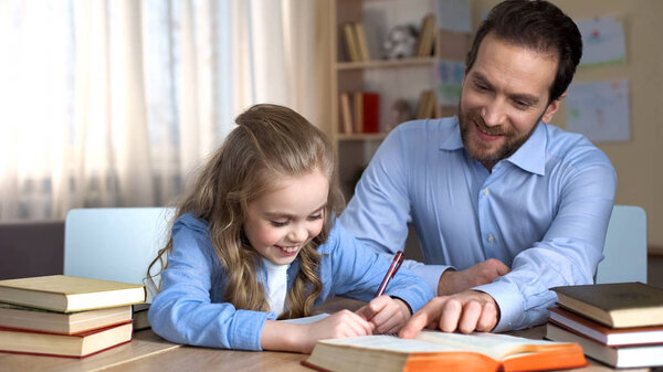 Smiling tutor helping little girl to learn new words, doing homework, education