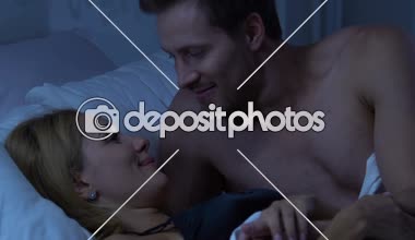 Yatakta kucaklayan ve kameraya bakarak mutlu evli çift bebek planlama