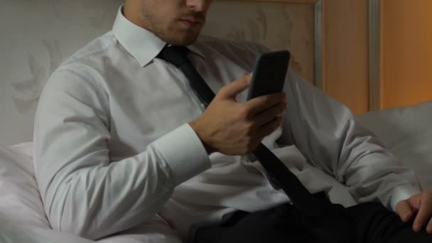男子躺在床上 在长天工作后在智能手机上阅读新闻和电子邮件 — 图库视频影像