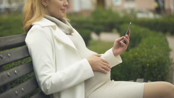 Glücklich Schwangere Frau Blättert Smartphone Fotos Entspannt Park Auf Bank — Stockvideo