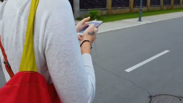 スマート フォンのアプリケーションを探して街を歩いてイヤホンの女性 — ストック動画