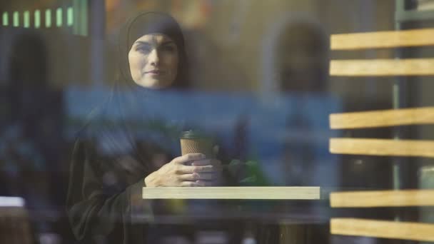 魅力的なイスラム教徒女性ウィンドウ内のカフェでコーヒーを飲む夢 — ストック動画
