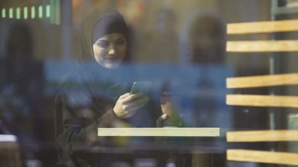 Όμορφη Μουσουλμανική Κυρία Πίνοντας Καφέ Και Κουβέντα Στο Τηλέφωνο Κάθεται — Αρχείο Βίντεο