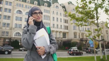 Kendine güvenen gülümseyen Müslüman kız öğrenci telefon ayakta Caddesi üzerinde konuşurken