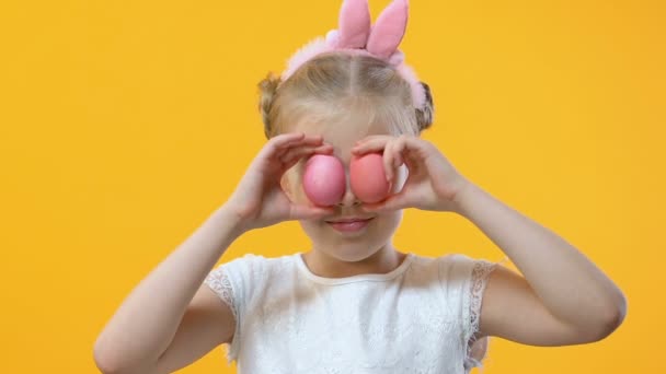 Menina Bonito Divertindo Colocando Ovo Colorido Aos Olhos Fundo Amarelo — Vídeo de Stock
