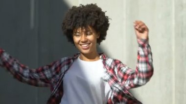 Gülümseyen ve sokak ve mutlu bir hayat üzerinde dans genç kıvırcık saçlı Afro-Amerikan Bayan