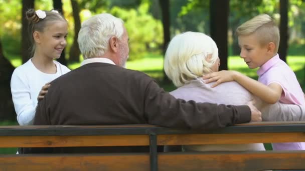 公園のベンチに座っている祖父母と楽しく話して少しかわいい子供たち — ストック動画