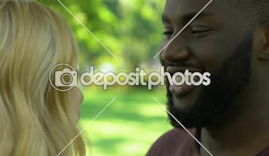 Romantic date of happy mixed race couple smiling and hugging in park, close up