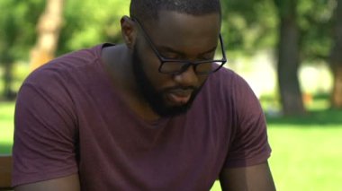 Afro-Amerikan adam bankta oturan ve onun smartphone üzerinde çalışmak için arama
