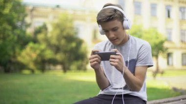 Cep telefonu, bağımlılık oyun oynarken parkta oturan kulaklıklar oyun