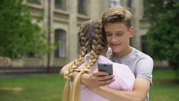 Εφήβου Χρησιμοποιώντας Κινητό Τηλέφωνο Ενώ Αγκαλιάζει Φίλο Απορροφάται Από Κοινωνικά — Αρχείο Βίντεο