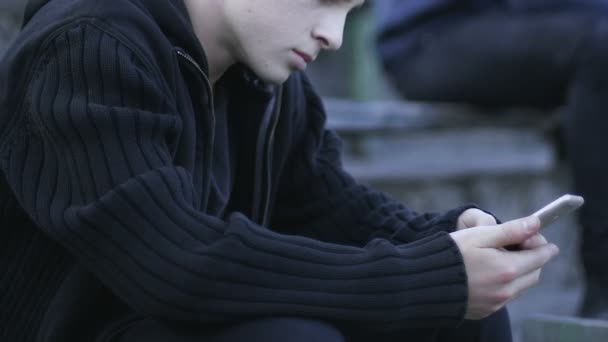 十几岁的男孩坐在户外玩智能手机上的游戏 小工具成瘾 — 图库视频影像
