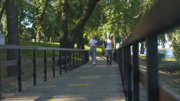 アクティブな年金受給者ヨガ マット広告水ボトルで公園を歩いてトレーニング — ストック動画