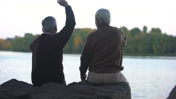 Пожилые Пенсионеры Бросают Камни Воду Сидят Берегу Реки Отдыхают Выходным — стоковое видео