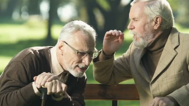 年龄大的退休老人 坐在公园的长椅上 听朋友说话时听力有问题 — 图库视频影像