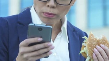 Telefon, yoğun yaşam tarzı nedeniyle kötü beslenme kullanırken burger yiyen kadın
