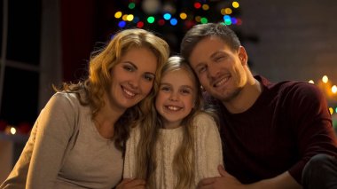 Genç aile sarılma, gülümseyen ve kamera, Noel'de birlikte mutlu isteyen