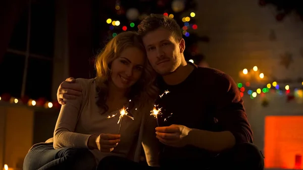 Pareja Feliz Con Luces Bengala Sentada Una Acogedora Habitación Cerca — Foto de Stock