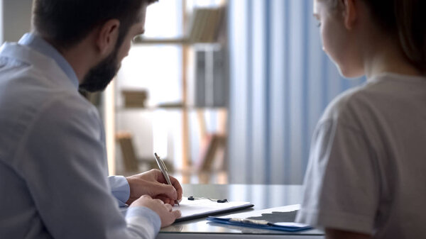 Therapist writing medical receipt to young female patient, health and treatment