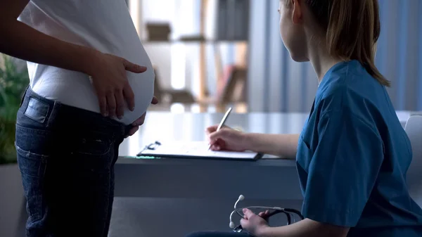 Νεαρός Γιατρός Γράφοντας Τις Σημειώσεις Μετά Από Εξέταση Έγκυο Γυναίκα — Φωτογραφία Αρχείου