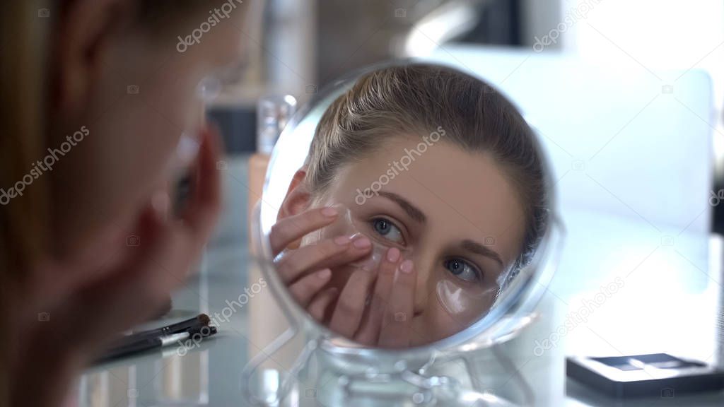Woman putting gel patches under eyes, moisturizing skin, anti-wrinkles effect