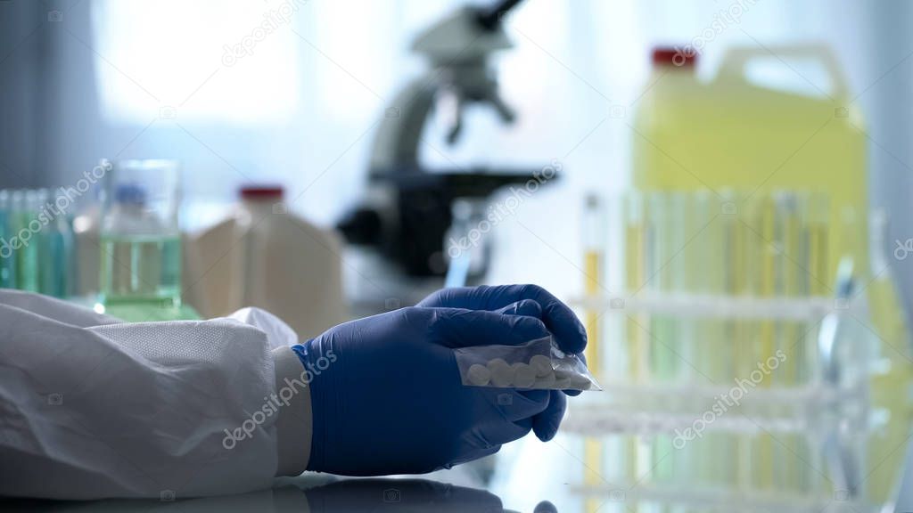 Lab worker holding plastic bag with pills inside clandestine pharmaceutical labs