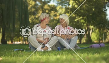 İki kadınla çimenlerin üzerinde alıştırmalar, sonra otururken bir yukarı başparmak olumlu gösterilen