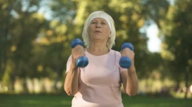 Park, spor oranım dumbbells ile egzersizleri yapıyor yorgun kadın kıdemli
