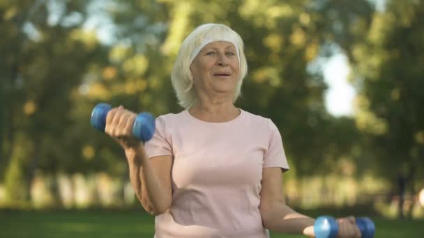 微笑的老太太在公园的阳光明媚的日子里用哑铃做健身 生活方式 — 图库视频影像