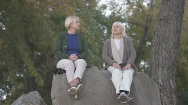Yaşlı anne ve onun olgun kızı parkta taşlar üzerinde oturan ve konuşurken