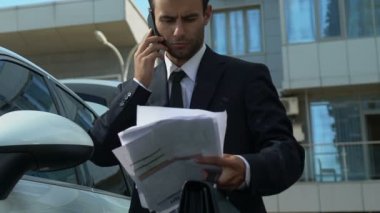 Business person talking on phone near car, solving financial issues of company