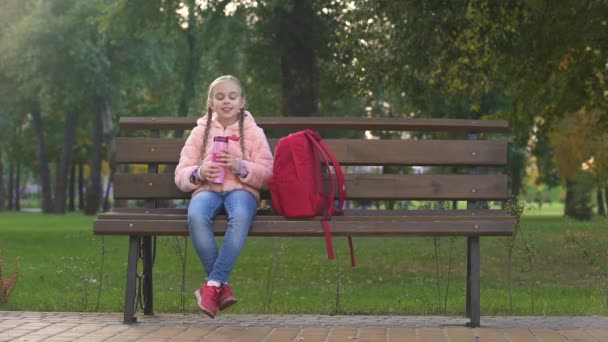 リュックサックとしてベンチに座って魔法瓶カップからお茶を飲む幸せな女子高生 — ストック動画