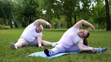 Fat couple having workouts in park together, beginners in weight loss program clipart