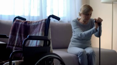 Kanepe ve oda, yalnızlık içinde ağlayan, boş tekerlekli sandalye üzerinde oturan Engelli Kadın