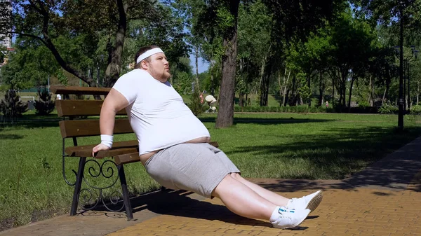 Obese young man exercising on bench, outdoor workouts, struggle to slim down