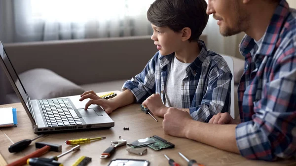 父亲和孩子坐在桌子上 一起在笔记本电脑上搜索 视频教程 — 图库照片